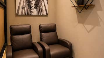 Una habitación con dos sillones de cuero reclinables, un estante para plantas en la pared y una gran foto enmarcada de palmeras.