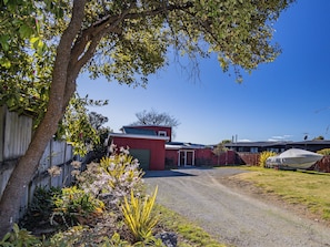 Un quartier résidentiel avec une allée en gravier menant à un garage rouge, entouré de verdure et d’une clôture en bois.