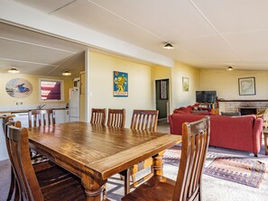 Un coin repas avec une table et des chaises en bois, une cuisine en arrière-plan, un canapé rouge et une cheminée.