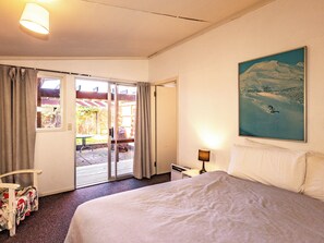 A hotel room with a bed, a painting, a lamp, and a sliding glass door leading to an outdoor area.