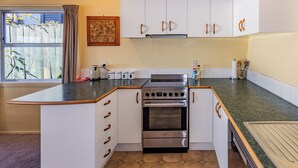 A compact kitchen with a built-in stove, a coffee maker, and a toaster. - Moeroa - Wharewaka Holiday Home (Wharewaka)