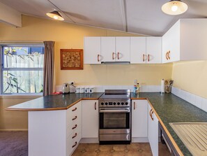 A compact kitchen with a built-in stove, a coffee maker, and a toaster. - Moeroa - Wharewaka Holiday Home (Wharewaka)