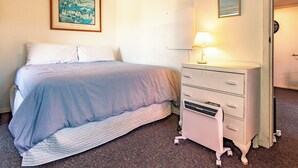 Un dormitorio con cama, cómoda, lámpara y un cuadro en la pared.