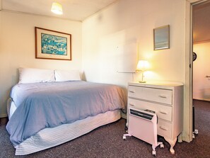 Un dormitorio con cama, cómoda, lámpara y un cuadro en la pared.