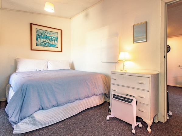 Une chambre à coucher avec un lit, une commode, une lampe et un tableau encadré au mur.