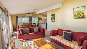 A living room with two red sofas, a wooden coffee table, and a wicker chair. - Moeroa - Wharewaka Holiday Home (Wharewaka)