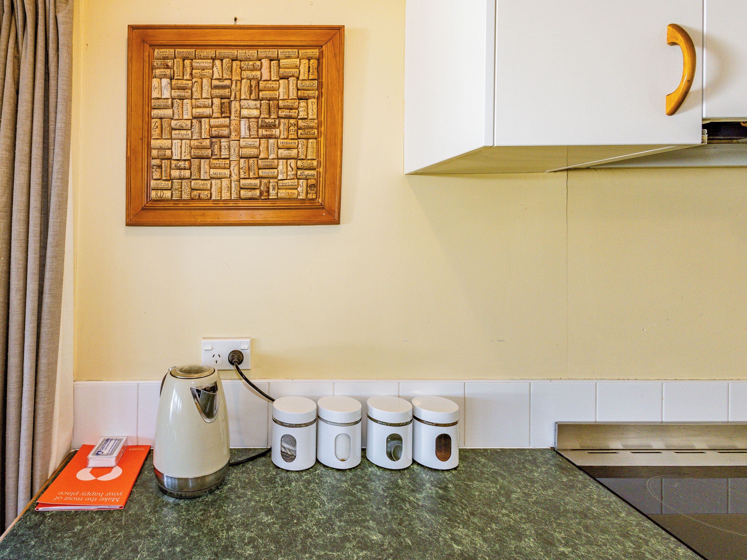A kitchen with a corkboard wall art, a kettle, and four white containers on the counter.