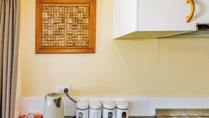 Una cocina con un mural de corcho, una tetera y cuatro recipientes blancos sobre la encimera.