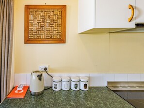 Una cocina con un mural de corcho, una tetera y cuatro recipientes blancos sobre la encimera.