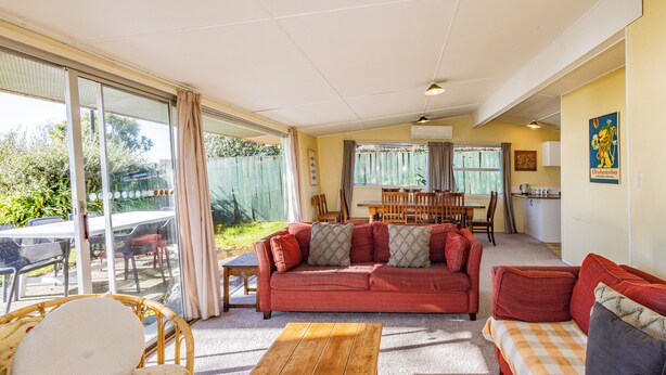 A spacious living area with a red sofa, a wooden coffee table, and a dining table set for four. - Moeroa - Wharewaka Holiday Home (Wharewaka)