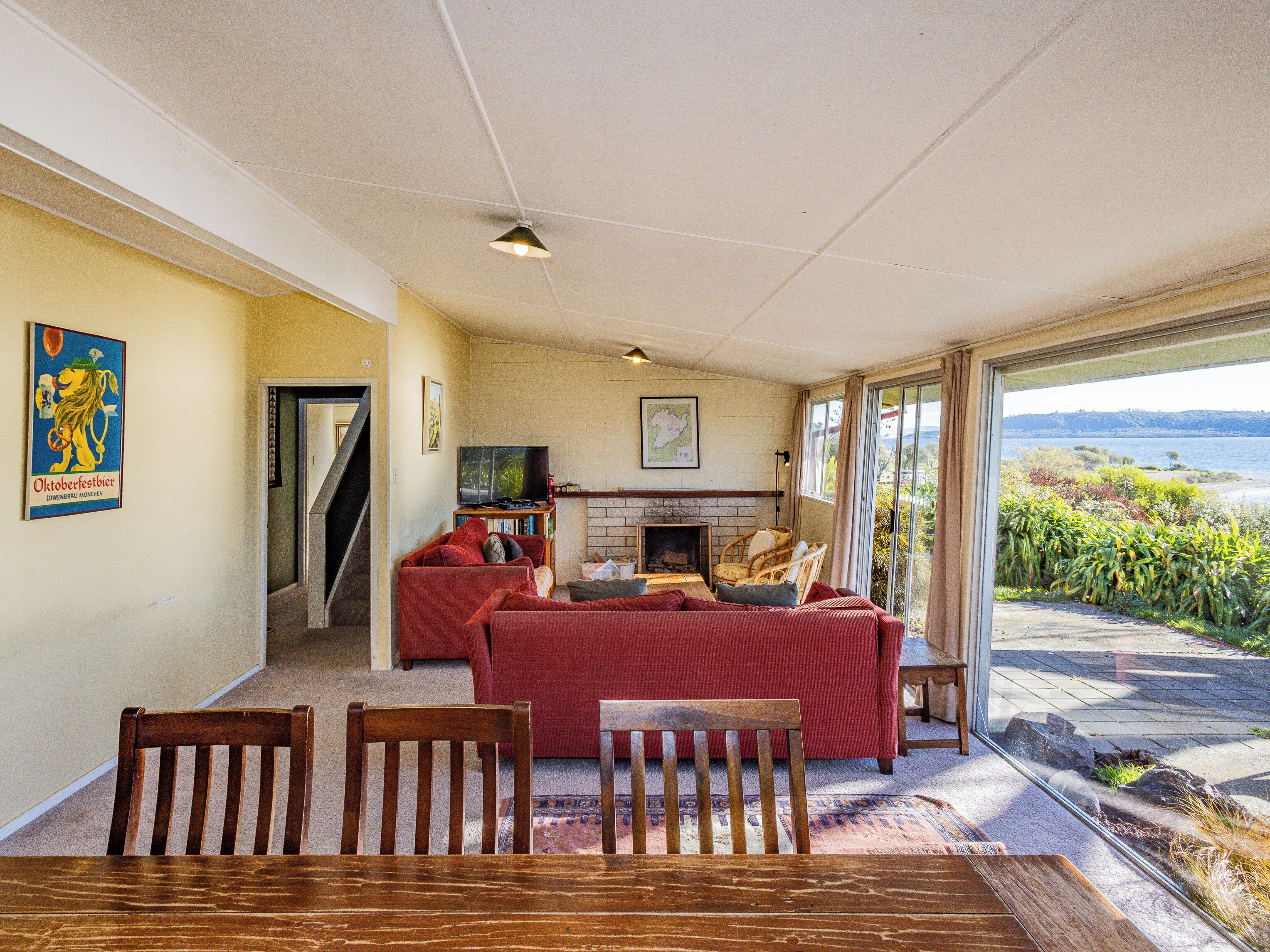 A living room with a red sofa, a television, and a fireplace. There is a dining table with chairs and a view of the sea through large windows.