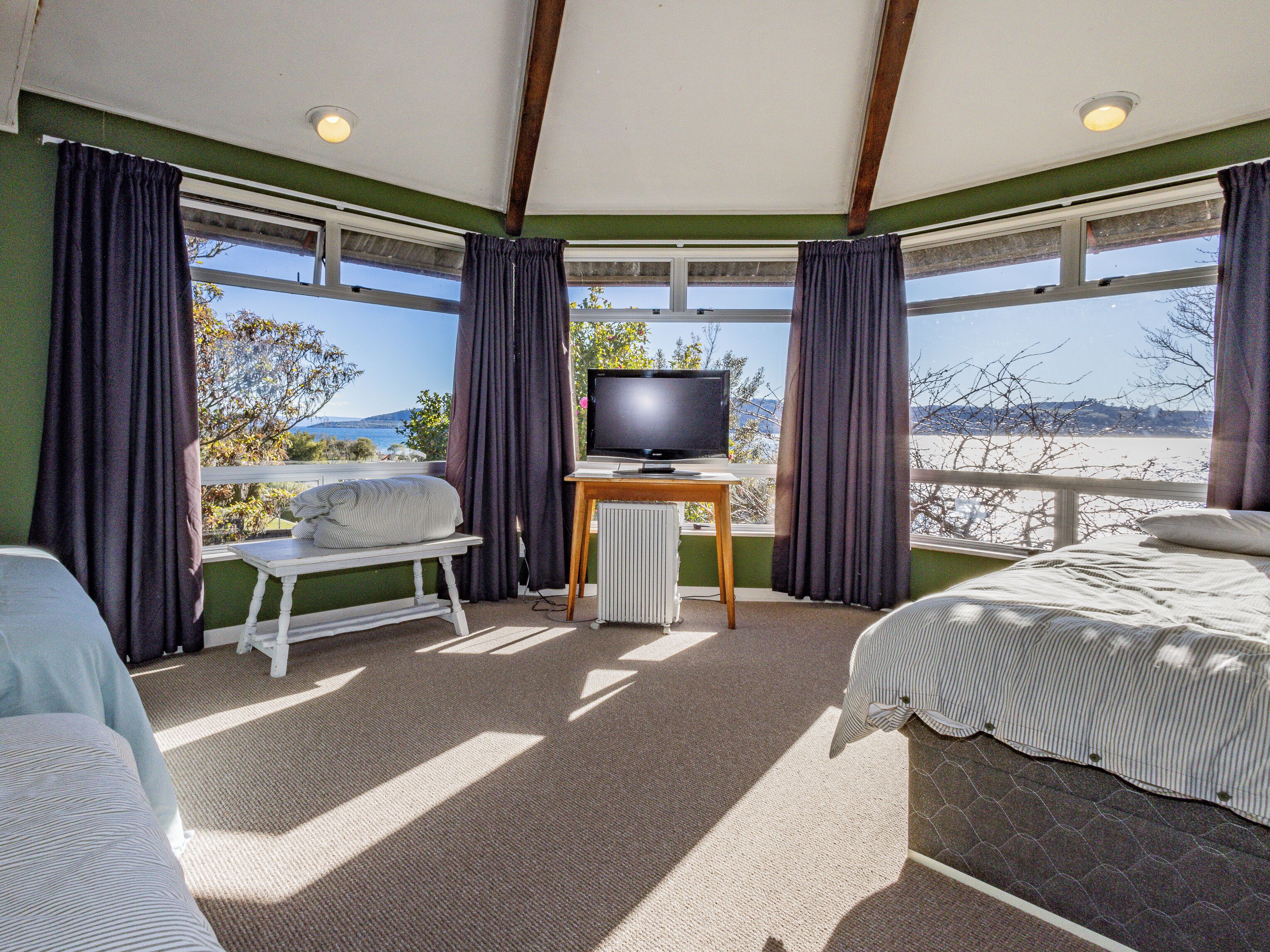 A room with a bed, a small table with a television, and a view of the beach.