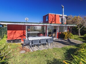A modern house with a red exterior, a satellite dish, a barbecue area, and a patio with a table and chairs. - Moeroa - Wharewaka Holiday Home (Wharewaka)