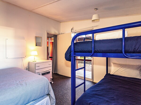 A dormitory room with bunk beds, a desk with a lamp, and a window.