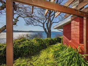 A covered outdoor area with a view of a body of water and distant hills. - Moeroa - Wharewaka Holiday Home (Wharewaka)