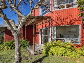 Un bâtiment rouge avec un porche couvert, une grande fenêtre donnant sur l’intérieur et un arbre au premier plan.