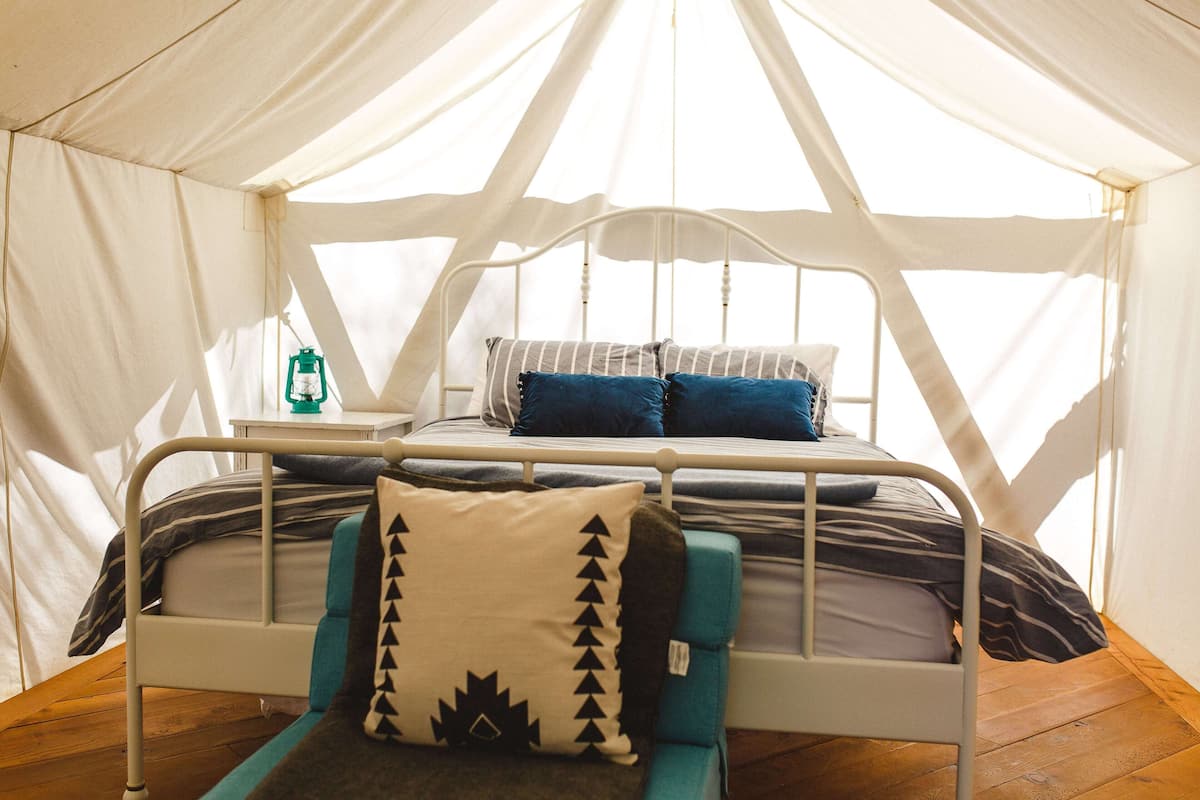 A tented accommodation with a single bed, a nightstand, and a lantern.