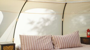 A tented room with a bed, striped pillows, a small wooden nightstand, and a lantern. - Smith Lake Farm (Black Creek)