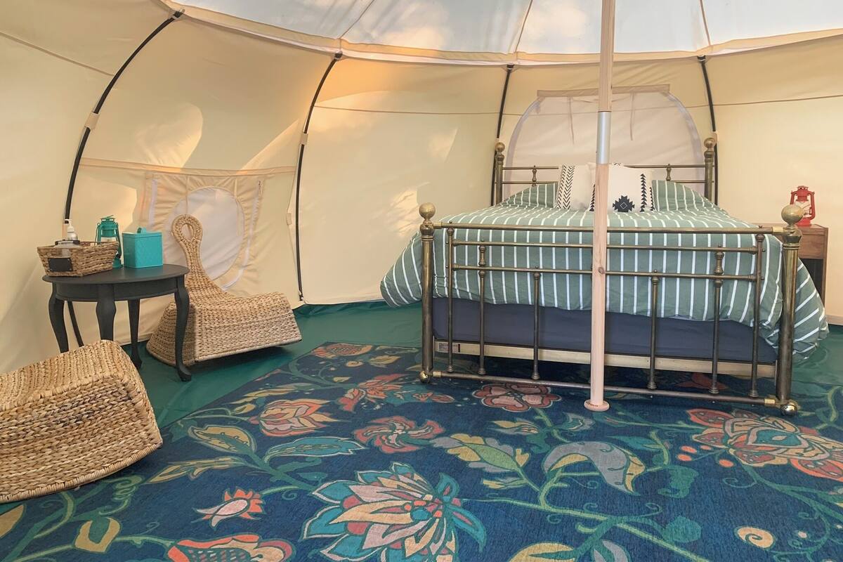 A tent with a bed, a table, and two wicker chairs.