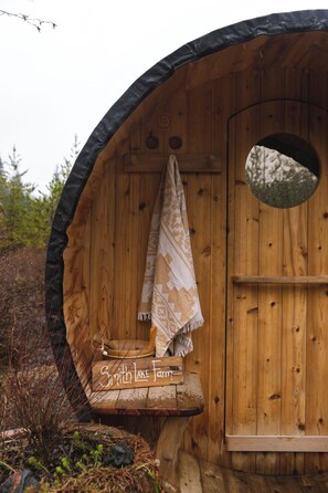 Eine Holzhütte mit einer runden Tür, einem kleinen Fenster und einer Bank mit einem Schild, auf dem 'Smith Lake Farm' steht.