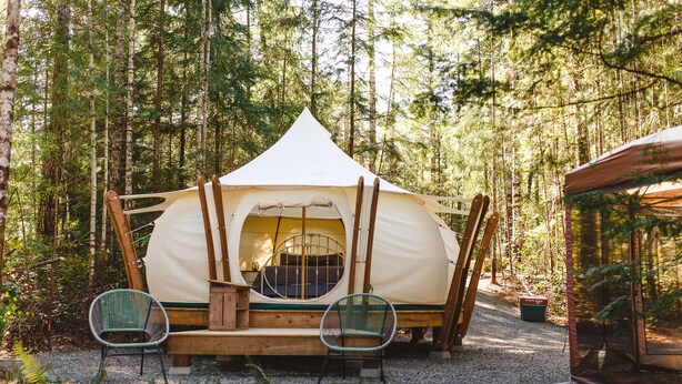 A tent with a circular entrance, surrounded by a forest. There are two chairs in front of the tent. - Smith Lake Farm (Black Creek)
