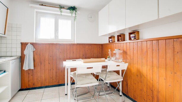 A compact kitchen with wooden paneling, a white countertop, and a window with a plant hanging above.