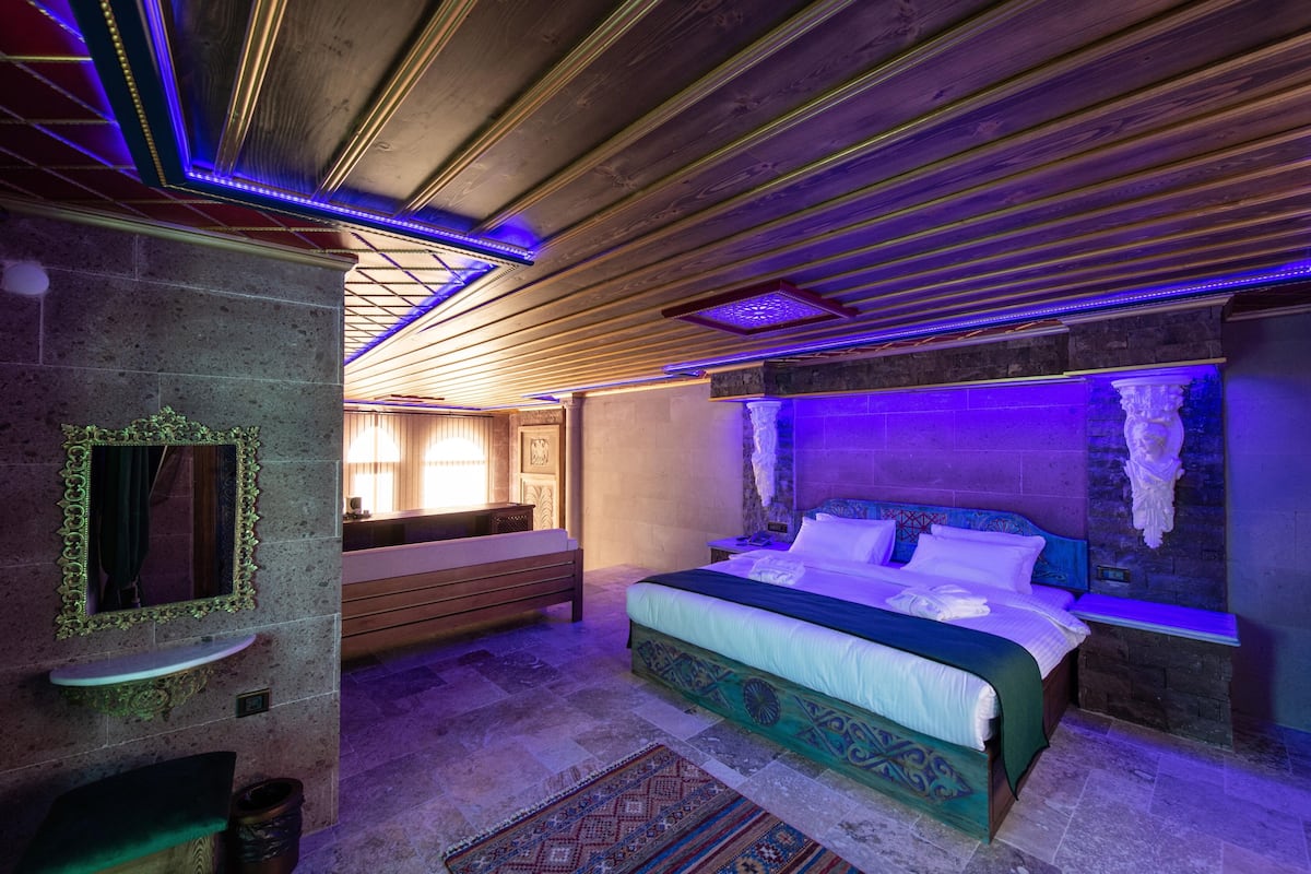 A bedroom with a large bed, a bench, a small table, and a mirror.