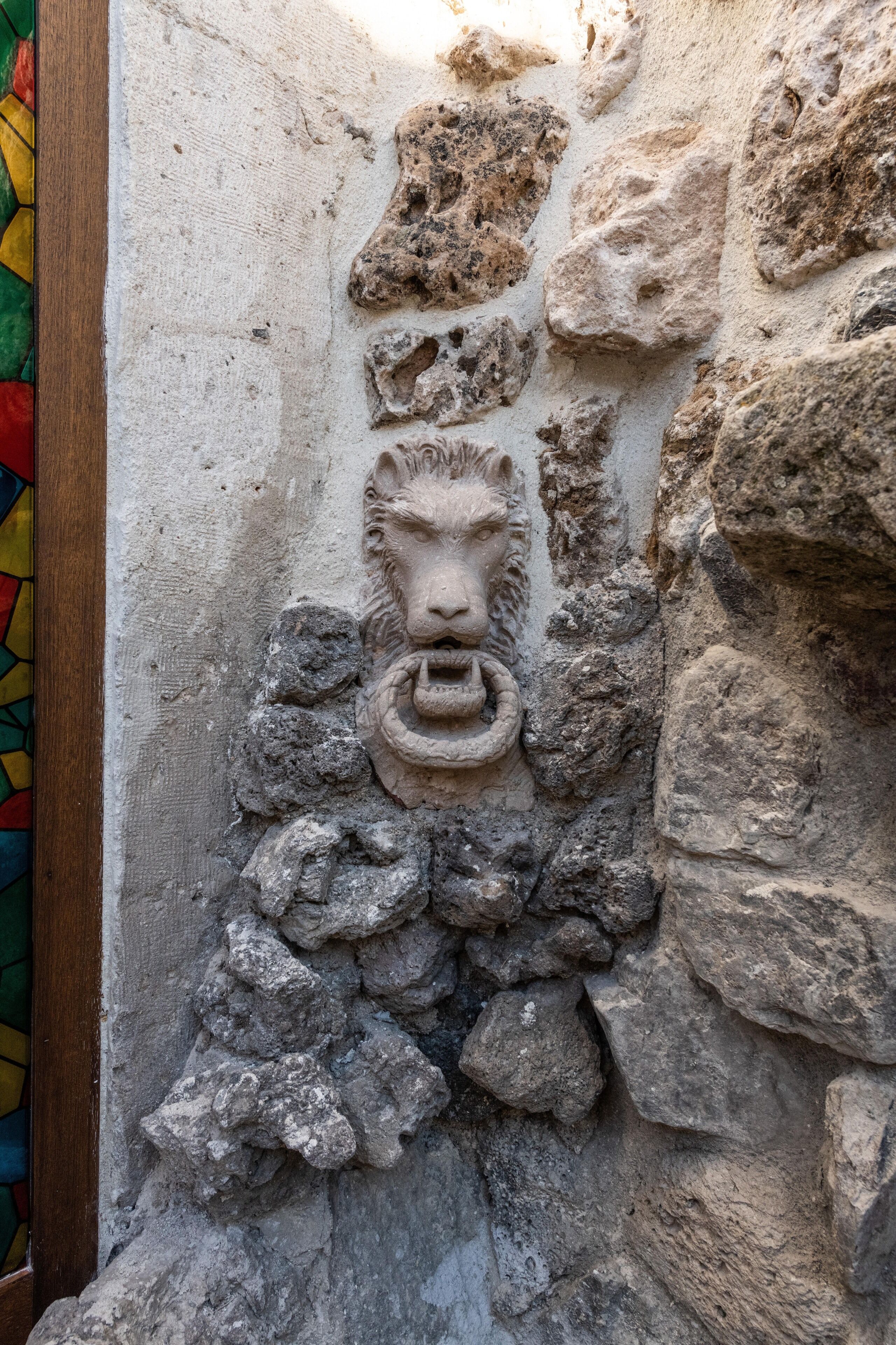 Eine Steinsäule mit einer Löwenkopf-Skulptur und rauher, unregelmäßiger Steinsetzung.