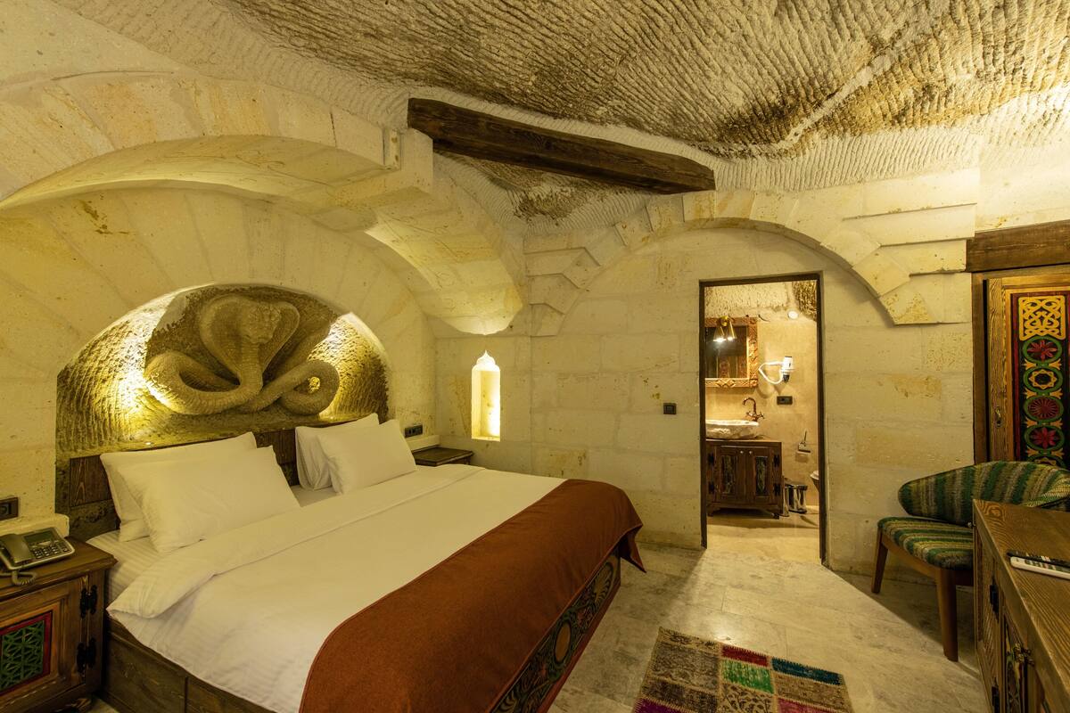 A stone-walled bedroom with a bed, a wooden nightstand, a telephone, and a chair.