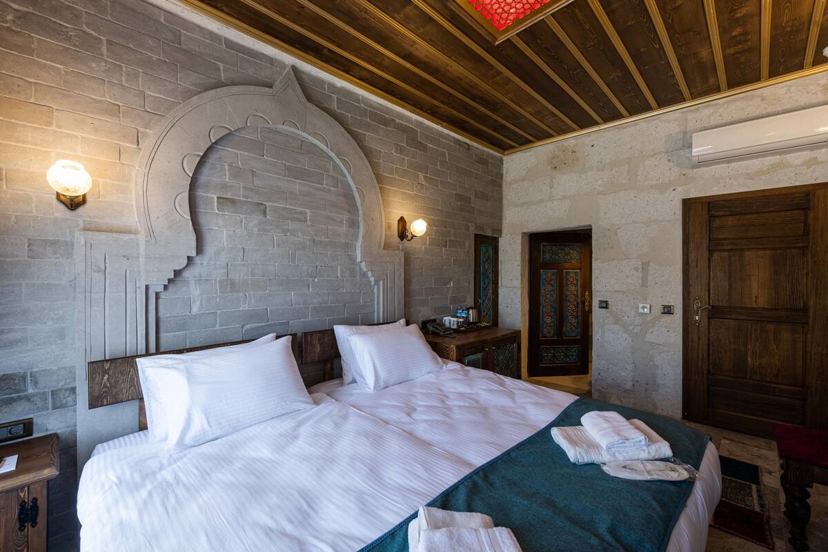 A hotel room with a large bed, a brick wall, and a wooden ceiling.