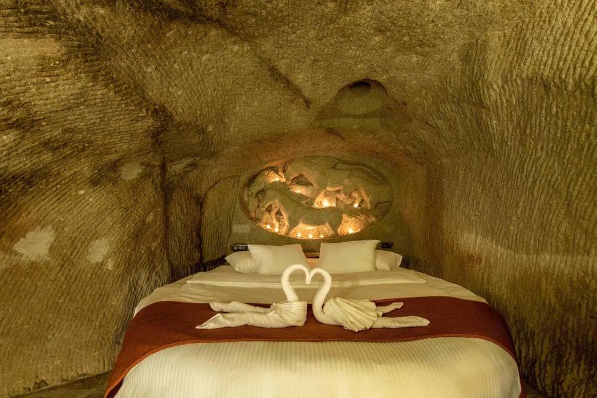 A cave-like room with a bed, pillows, and a heart-shaped towel arrangement.