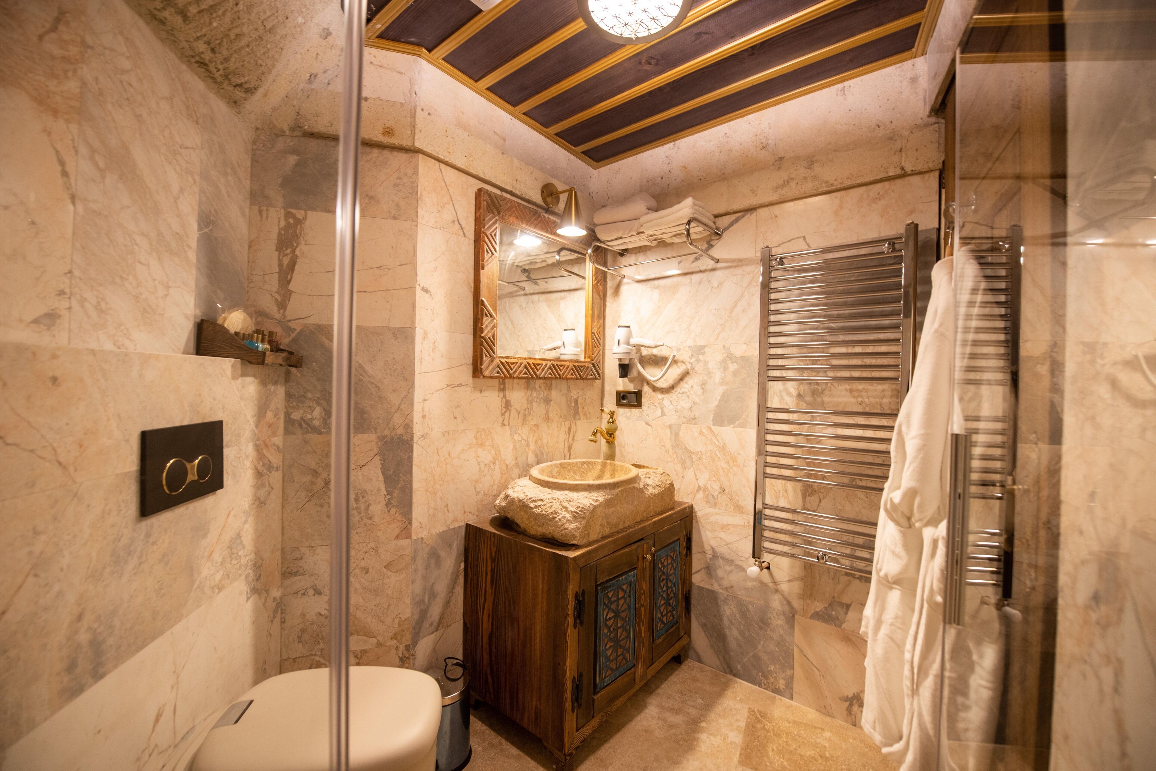 A bathroom with a marble wall, wooden vanity, a sink with a decorative basin, a towel rack, and a glass shower enclosure.