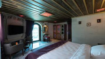 A hotel room with a large bed, a television, a fireplace, and a desk with a chair.