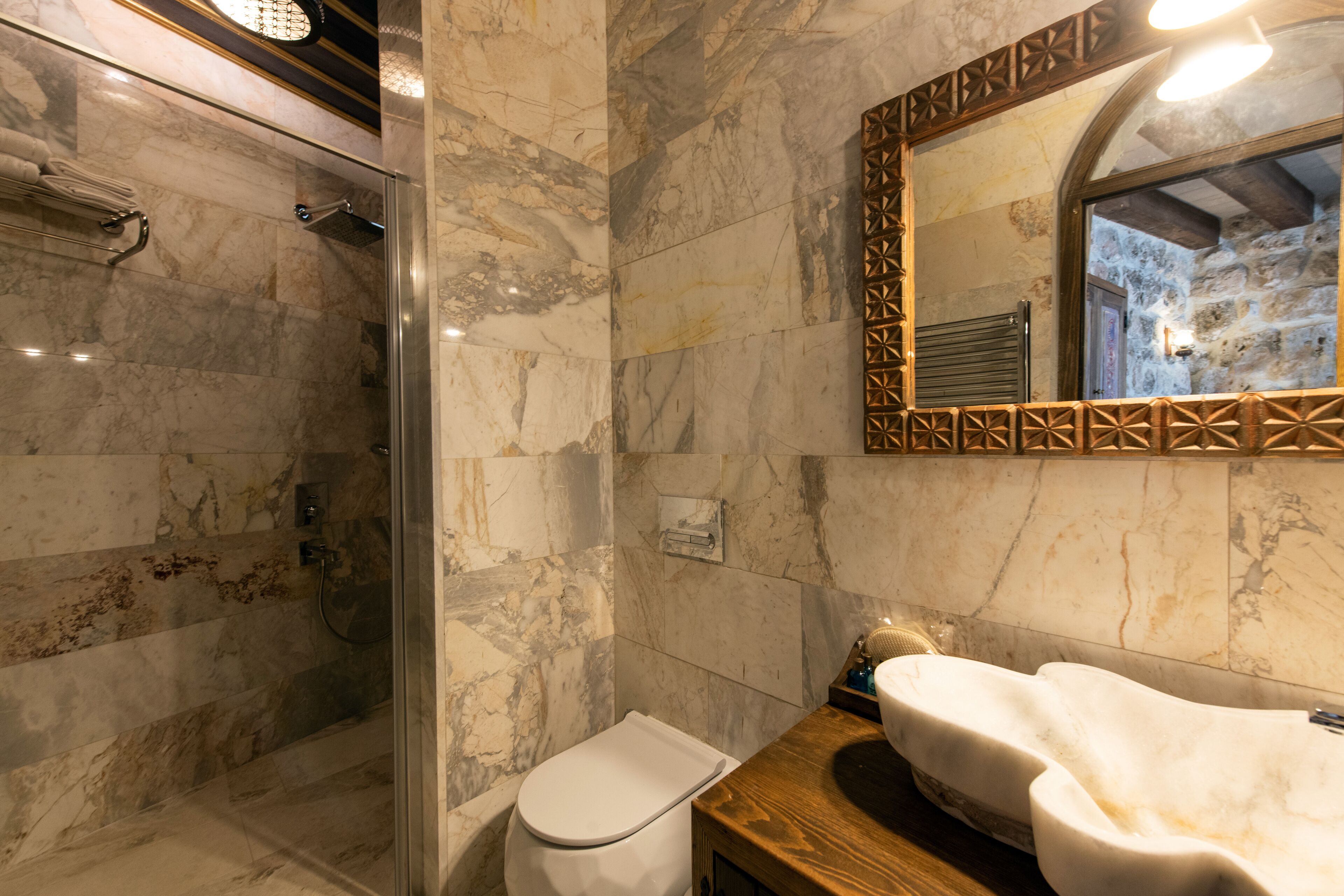 Een badkamer met een douche met glazen wand, een betegelde muur van marmer, een houten aanrecht en een wastafel met een handdoek.