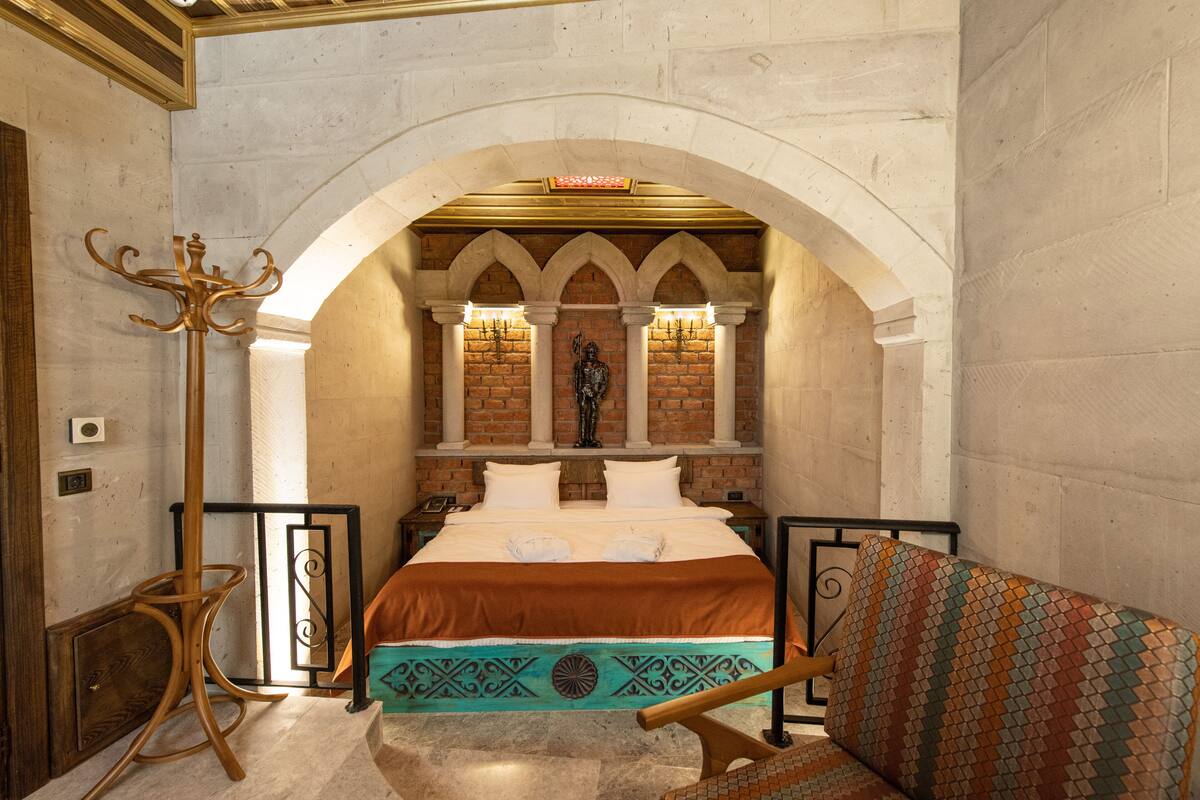 A room with a large bed, a wooden chair, a coat rack, and a decorative wall with a statue.