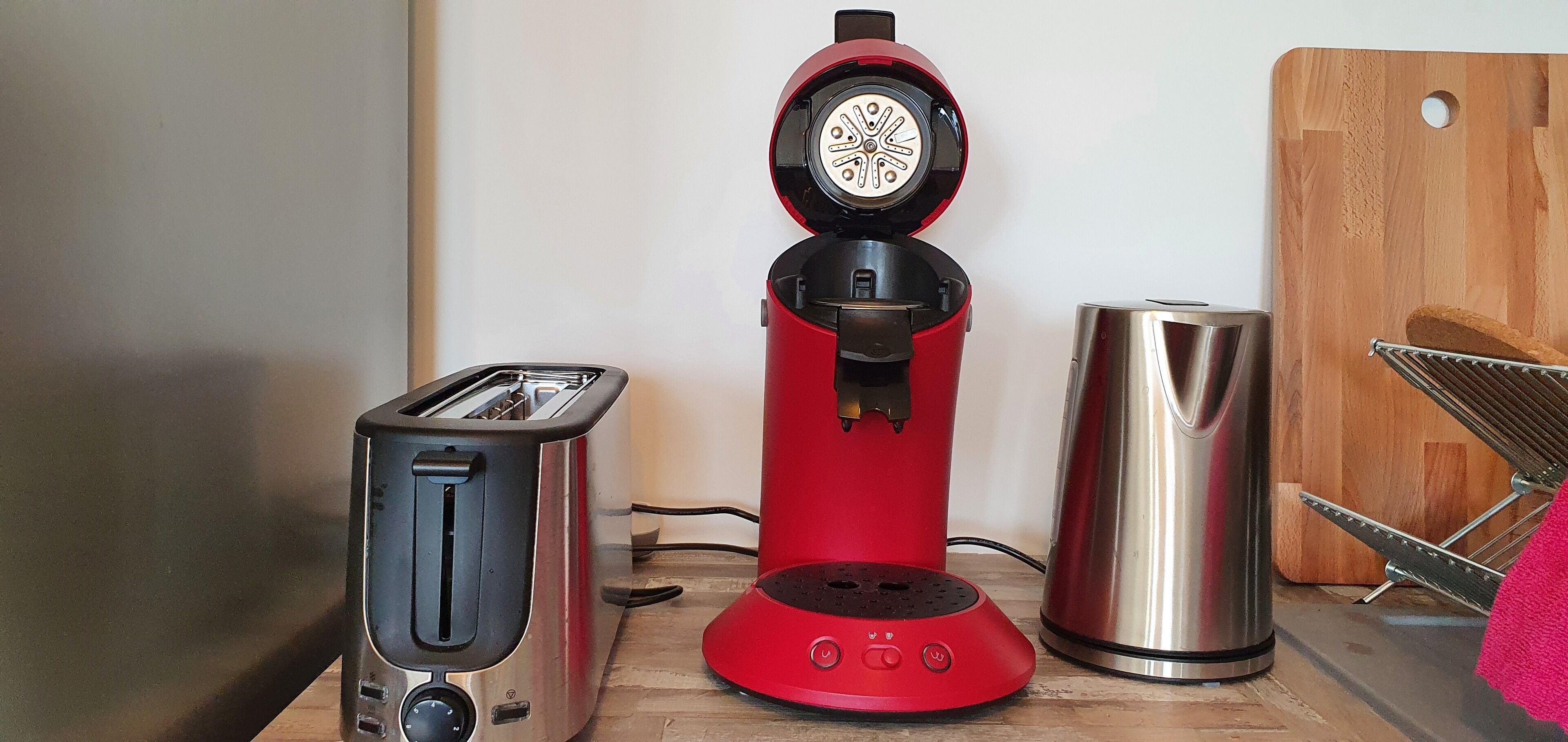 Una cocina con una cafetera roja, un tostador y un hervidor de acero inoxidable sobre una encimera de madera.