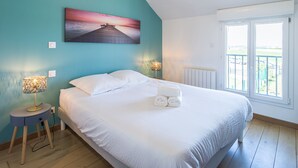A bedroom with a bed, two bedside lamps, a painting, a radiator, and a window with a view.