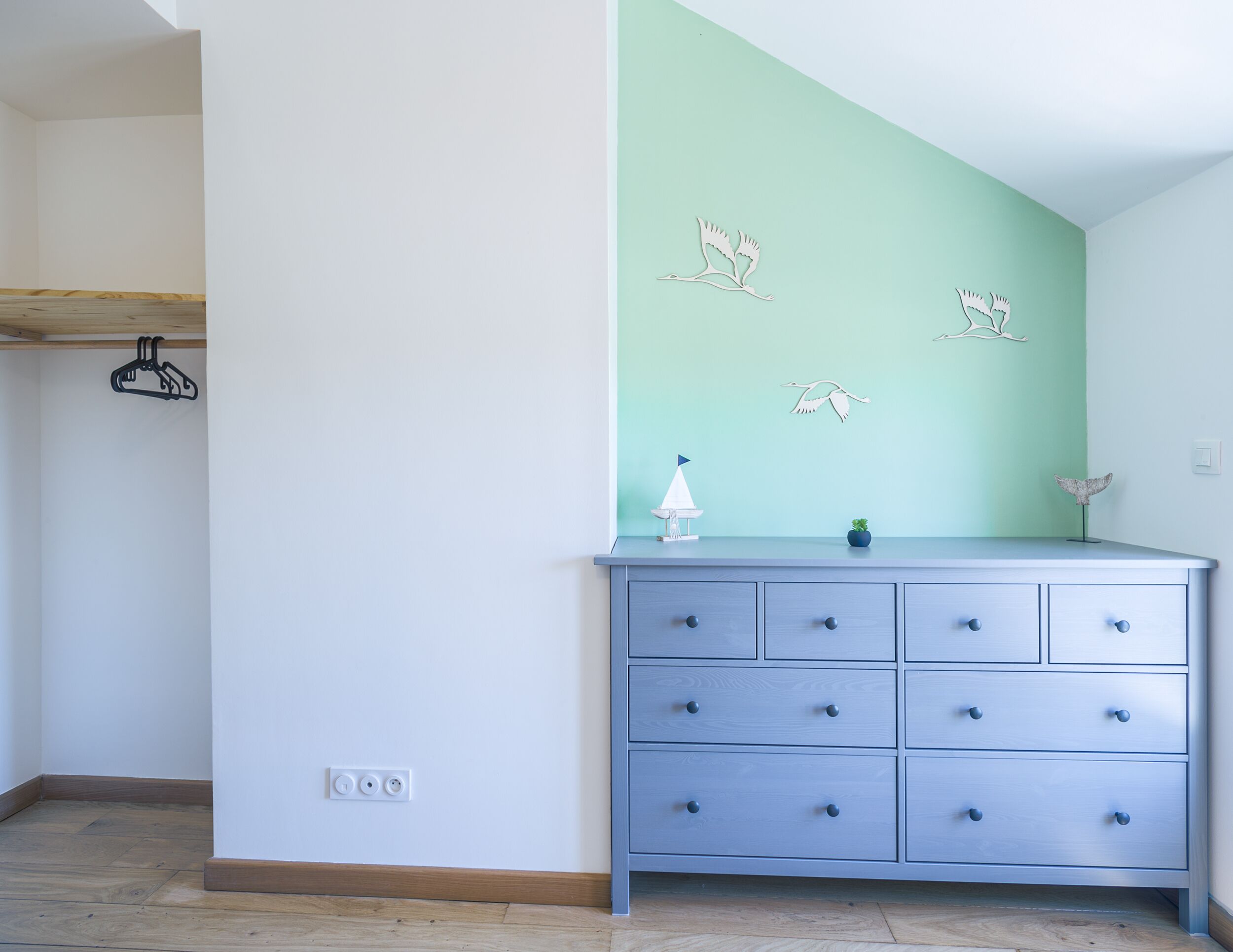 A room with a light blue dresser, a green accent wall, and a wooden shelf.