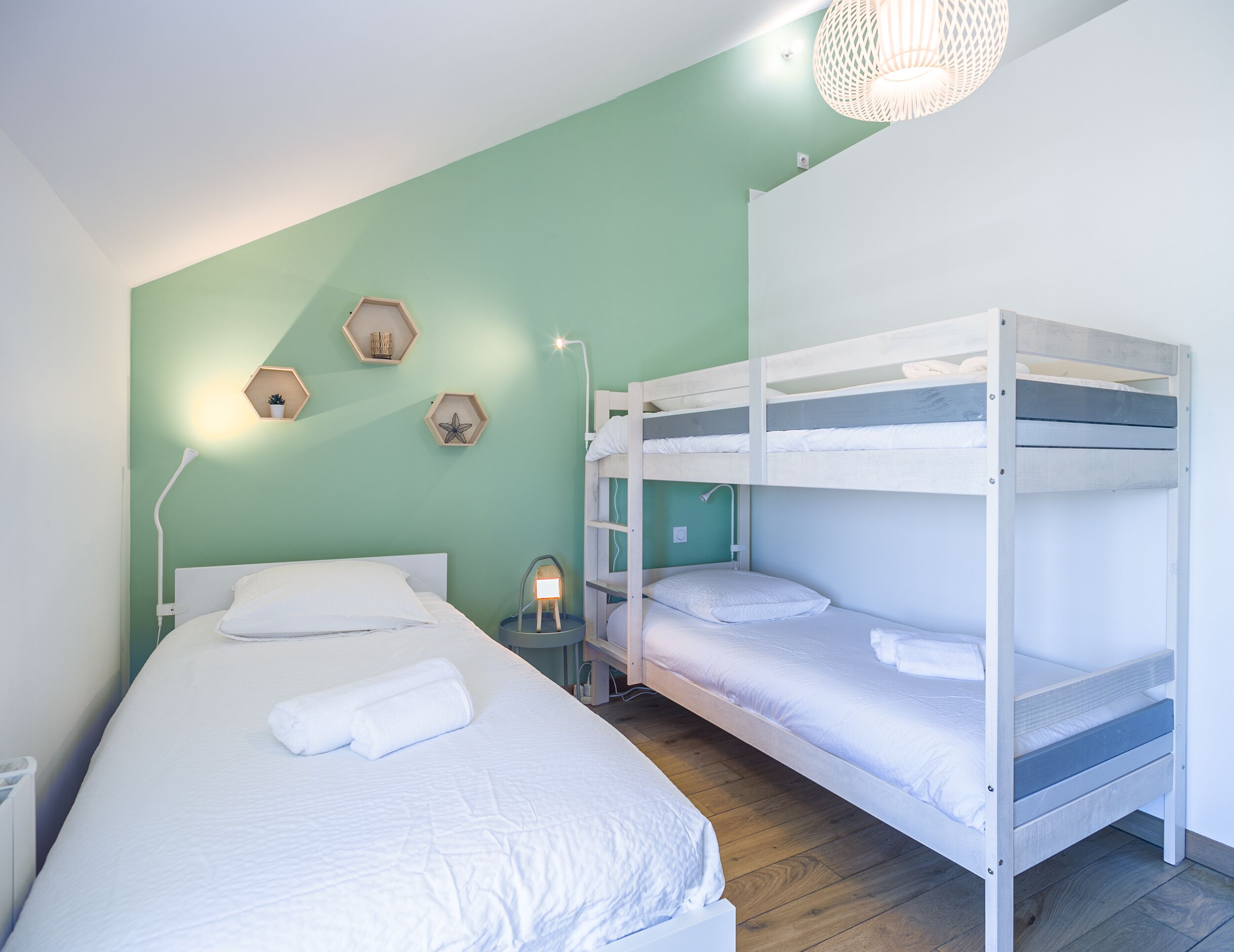 Une chambre avec un lit superposé, un mur vert, une table de chevet avec une lampe et deux éléments de décoration hexagonaux fixés au mur.