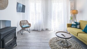 A living room with a sofa, a chair, a TV, a fireplace, and a large window with sheer curtains.