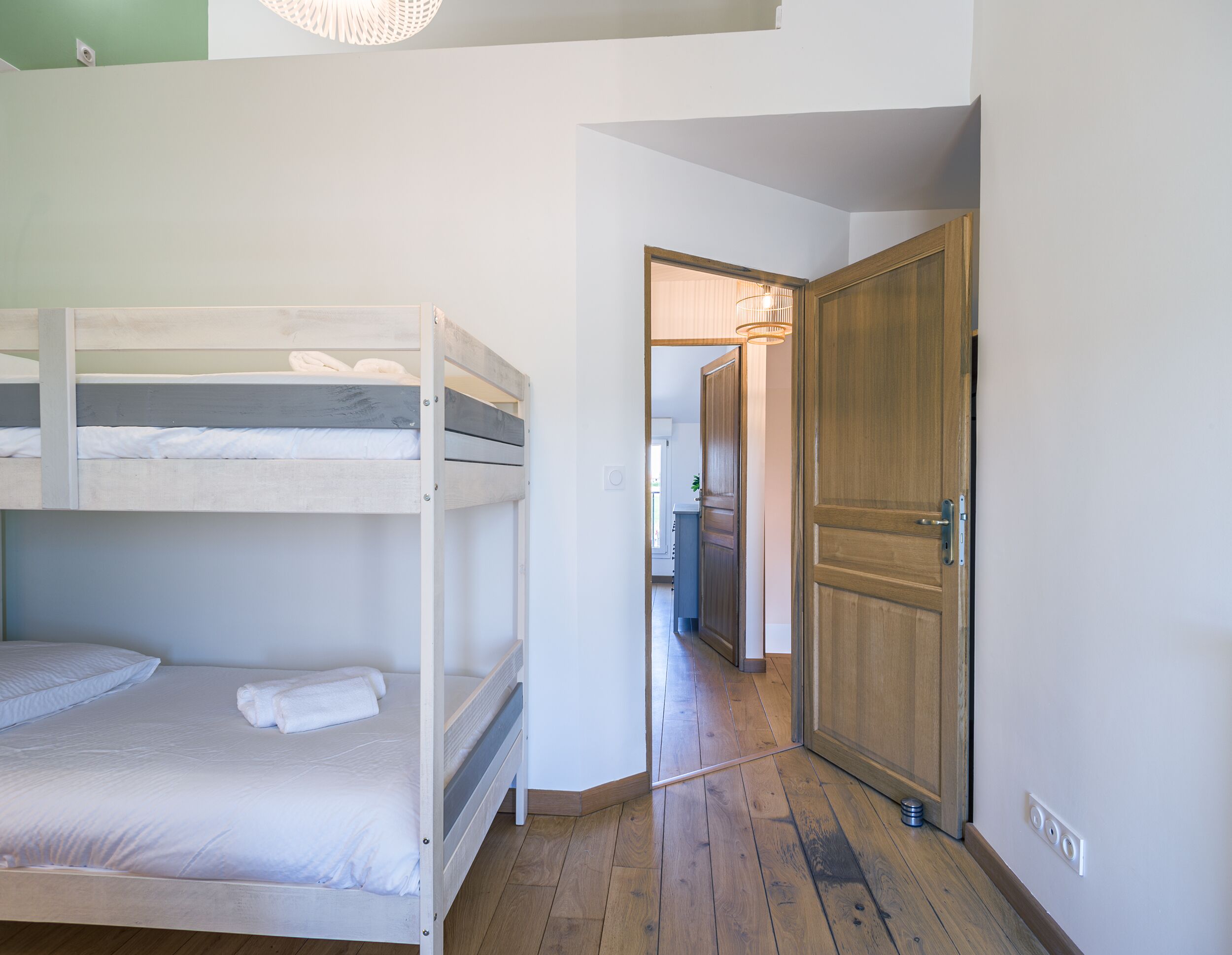 A room with bunk beds, a wooden door, and a hallway leading to another room.