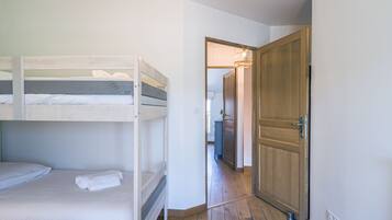 A room with bunk beds, a wooden door, and a hallway leading to another room.