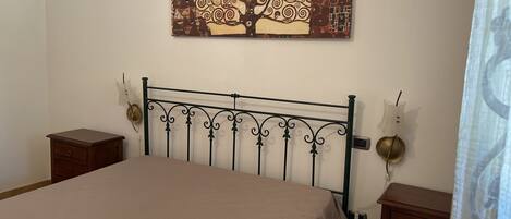 Une chambre à coucher avec un lit, une table de chevet, une lampe fixée au mur et un tableau représentant un arbre.