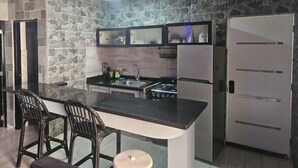 Una cocina con una isla central, taburetes de bar, estufa, refrigerador y una pared de acento de piedra.