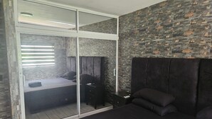 Un dormitorio con un amplio ventanal corredera que da a un balcón, cabecera oscura y una cama con almohadas.