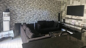 Una sala de estar con un sofá, un televisor de pantalla plana montado en la pared, un refrigerador y un salpicadero de azulejos.