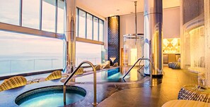 Ein moderner Poolbereich im Innenbereich mit Glaswänden, einer zentralen Wasserspiele und Sitzgelegenheiten am Poolrand.
