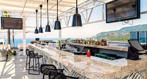 Eine Bar mit Meerblick, Barhocker und einer Theke mit verschiedenen Flaschen und Gläsern.