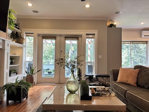 A living room with a piano, a sofa, a coffee table with a vase, and a bookshelf with plants.