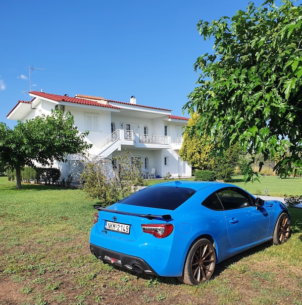 A blue sports car parked in front of a white house with a red roof, surrounded by greenery. - Silver Villa Raches, Sky Maisonette, 2 Floor Villa (Raches)
